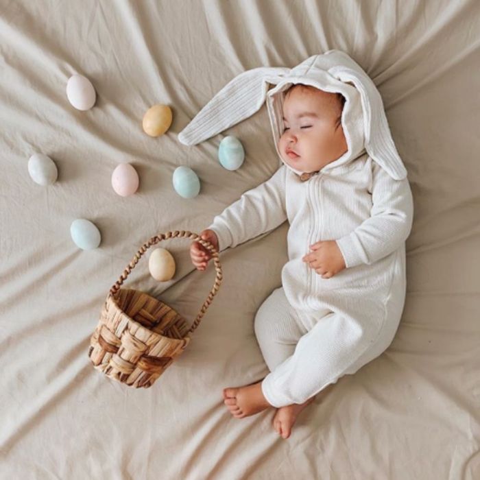 baby in bunny outfit sleeping with basket and easter eggs