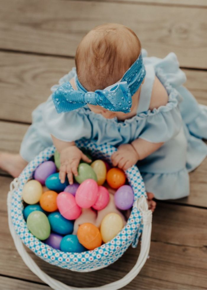 baby wearing blue dress and bow looking in an easter basket