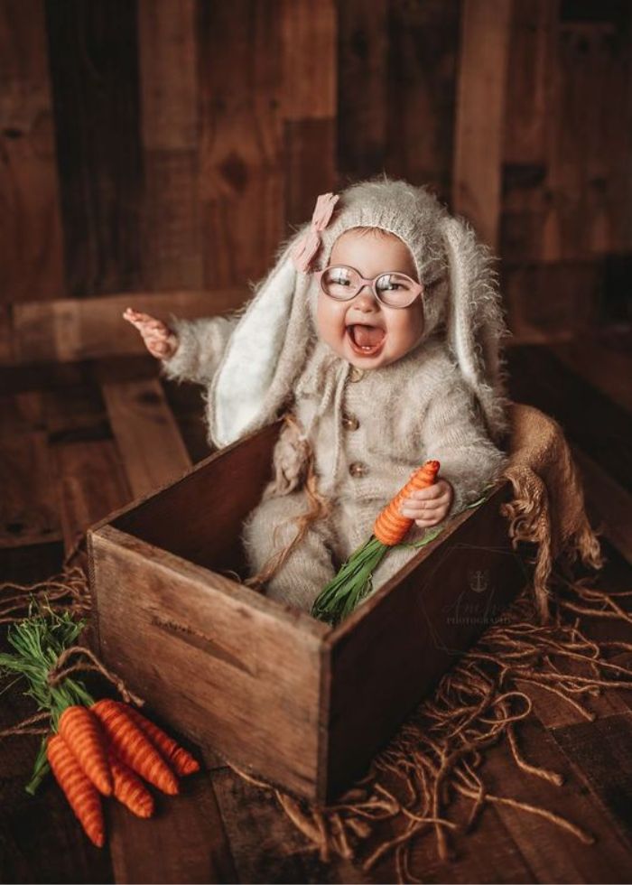 baby in a wooden crate wearing easter bunny outfit holding carrot