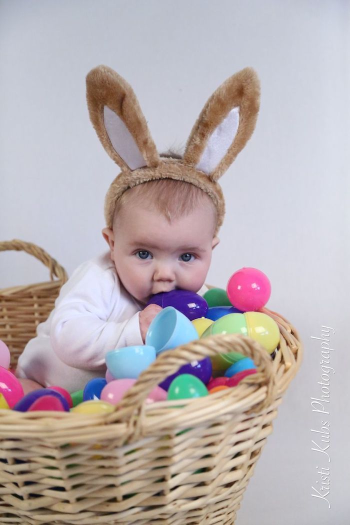 First Easter photo baby sitting in basket playing with multicolour plastic eggs