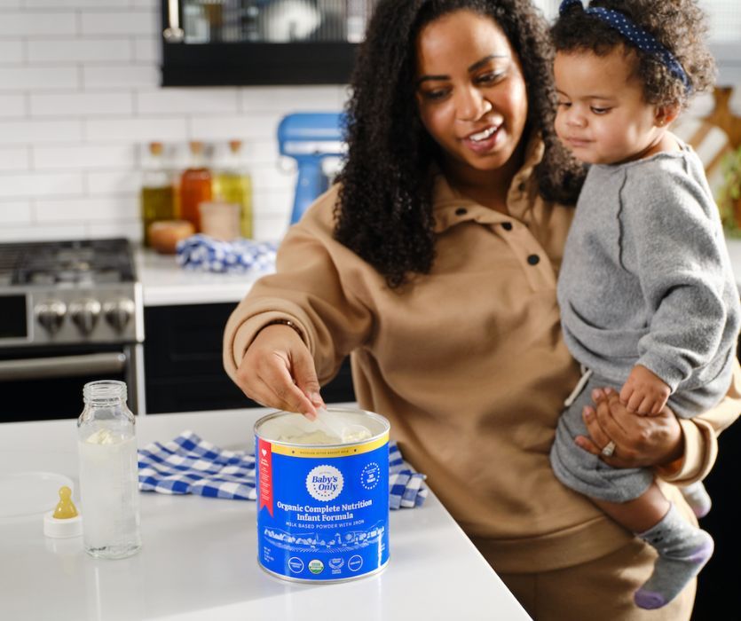 mom sweeps up formula while holding baby