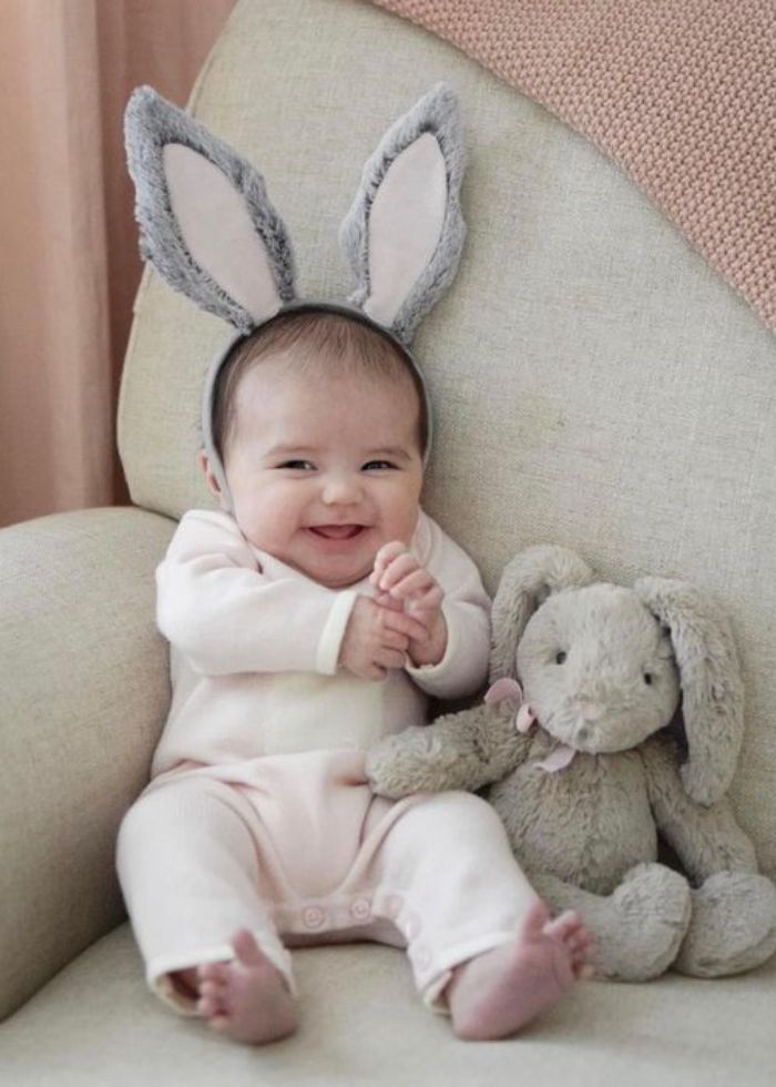 baby with bunny ears sitting on chair with grey rabbit