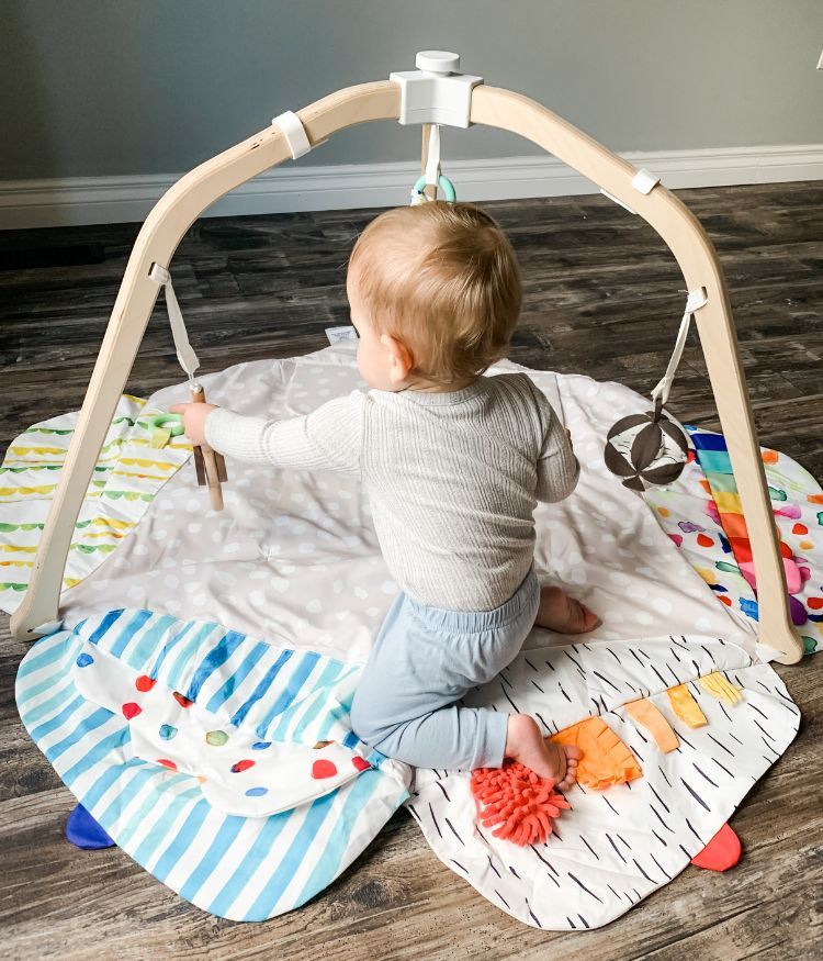 Baby kneeling on Lovevery play gym mat playing with hanging toy