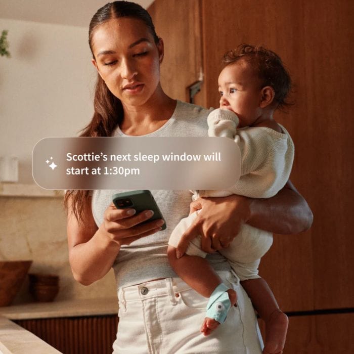 mom checking alert for owlet dream sock while holding her baby