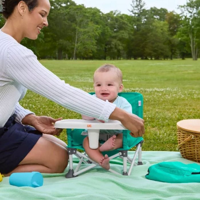 mom taking the tray off of a Portable Booster Seat her baby is sitting in at a picnic