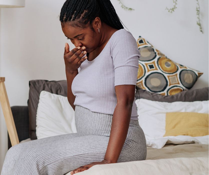 pregnant woman with morning sickness sitting on the edge of her bed