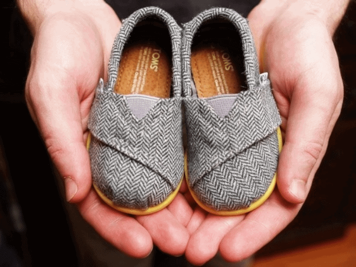 hands holding a pair of baby sized shoes as a baby gift that gives back to charity
