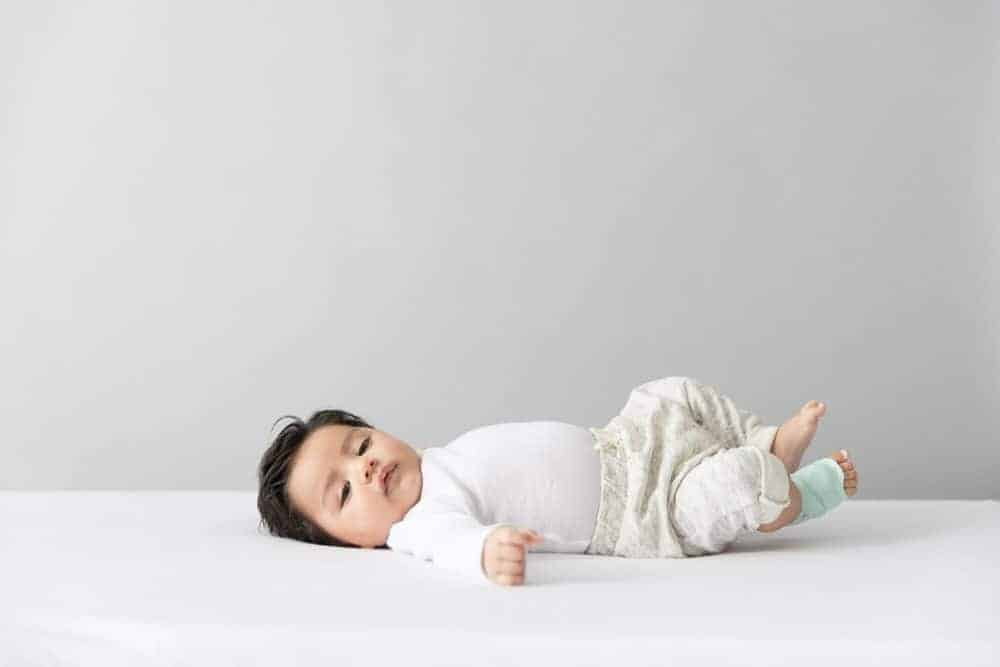 Baby laying on their back dressed in white clothes with Owlet Dream Sock on their foot