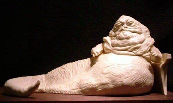 A detailed, cream-colored sculpture of Jabba the Hutt from Star Wars reclining against a dark background.