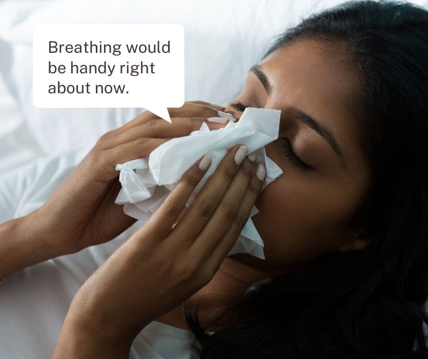 A person blowing their nose with a tissue. Text bubble: Breathing would be handy right about now.