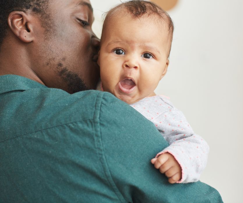 A father holding a fussy baby over his shoulder while the infant yawns.