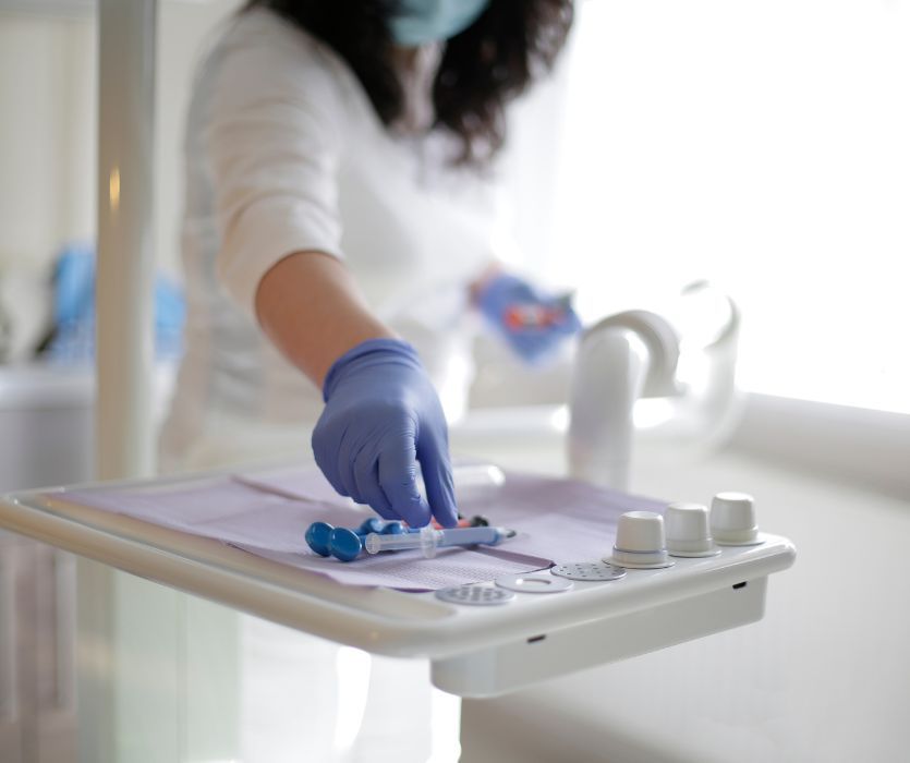 A dentist in blue gloves reaching for dental tools on a sterile tray.