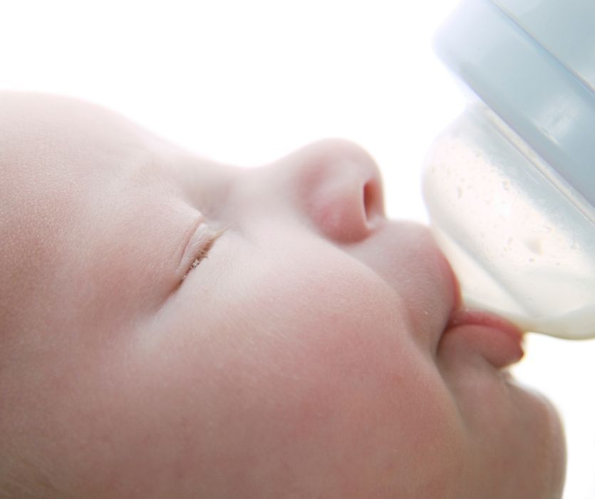 Close-up profile of a baby with eyes closed drinking milk from a bottle.