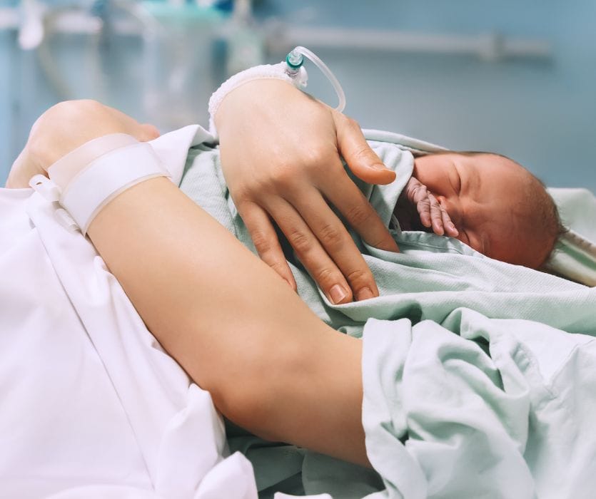 A mother in a hospital bed holds her newborn baby close to her chest for skin-to-skin contact.