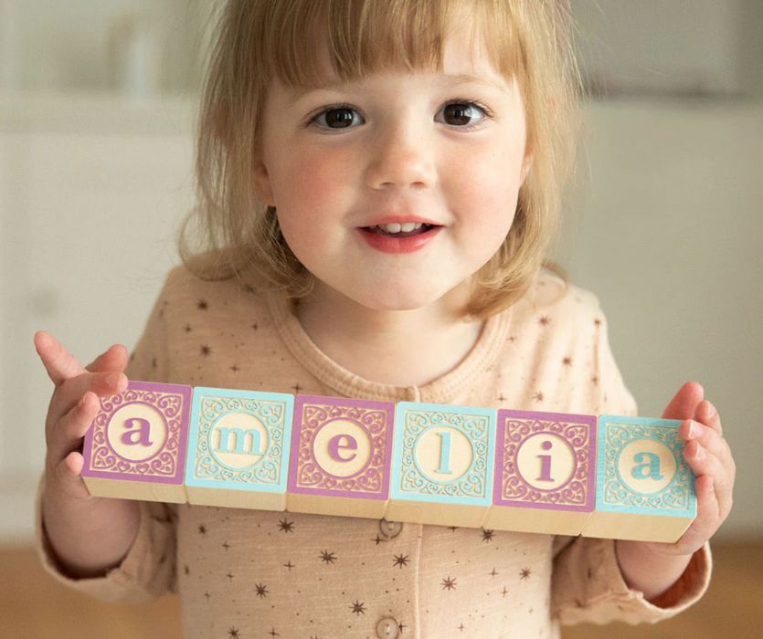 Young girl holding wooden toy blocks that spell the name Amelia.