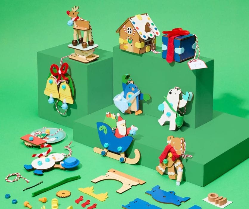 Assembled wooden Christmas ornaments including Santa in a sleigh, a reindeer, and a gingerbread house on green blocks.