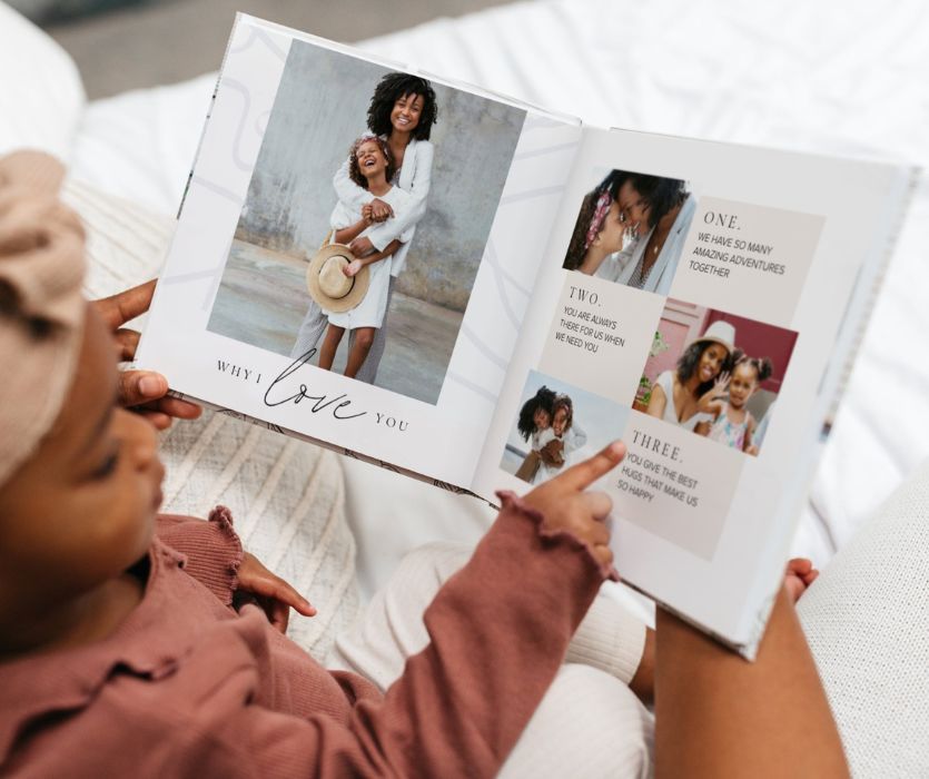 A child looking through a personalized photo book titled Why I Love You featuring family photos and text.