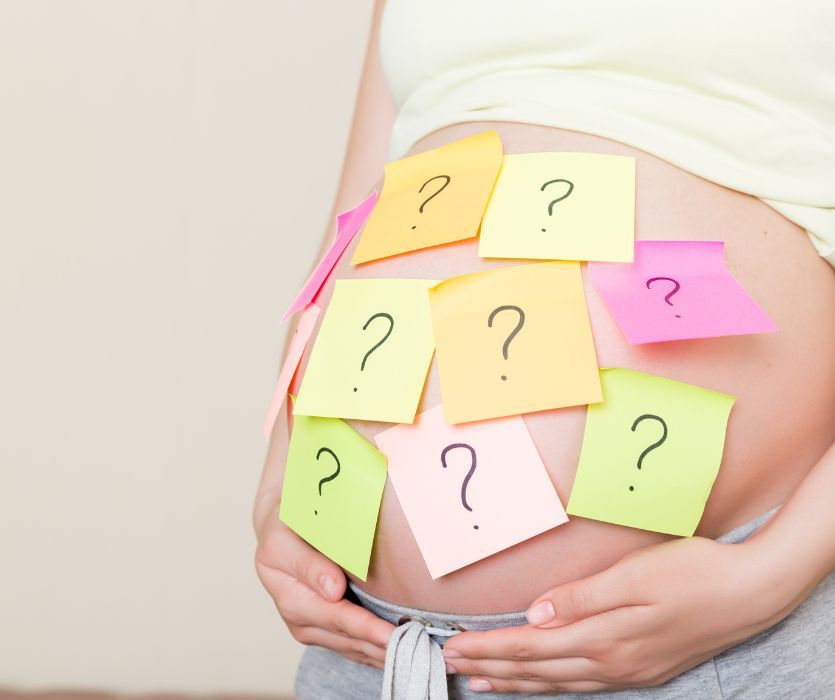 Colorful sticky notes with question marks covering a pregnant person's belly.