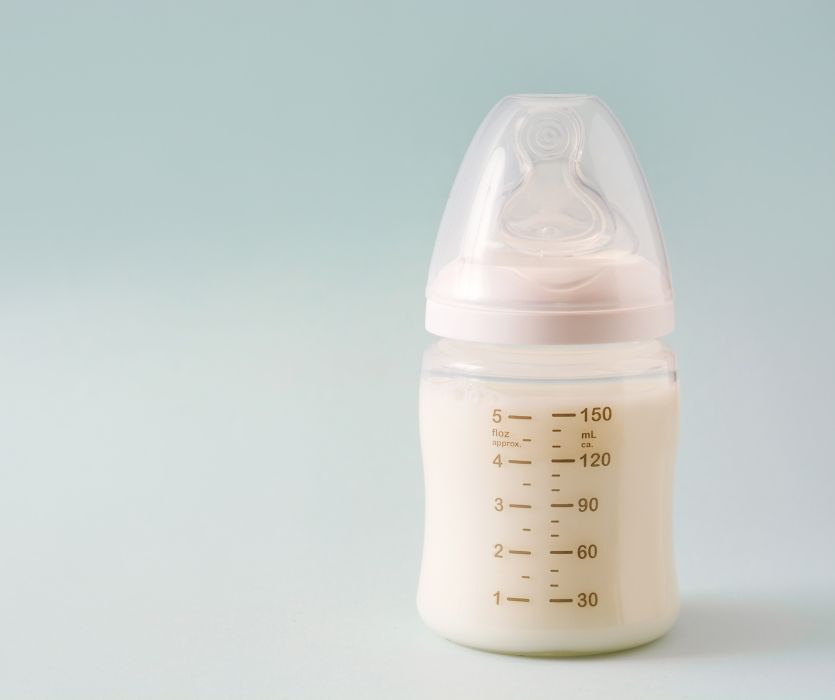 A baby bottle filled with breast milk against a light blue background.
