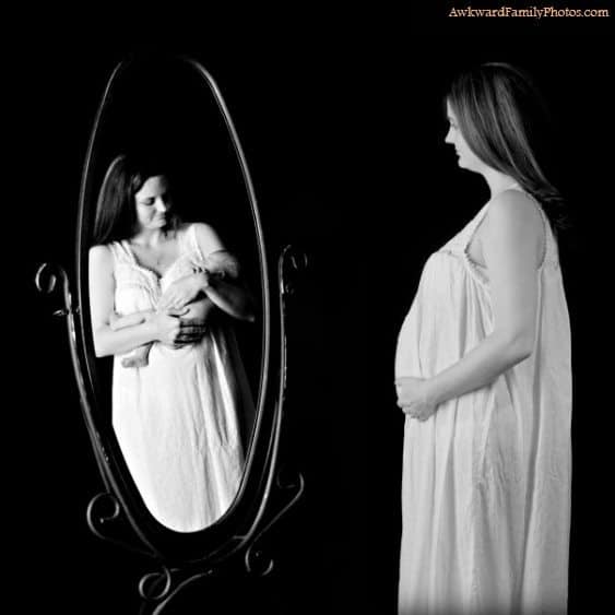 Black and white photo of a pregnant woman looking into a mirror that reflects her holding a baby.