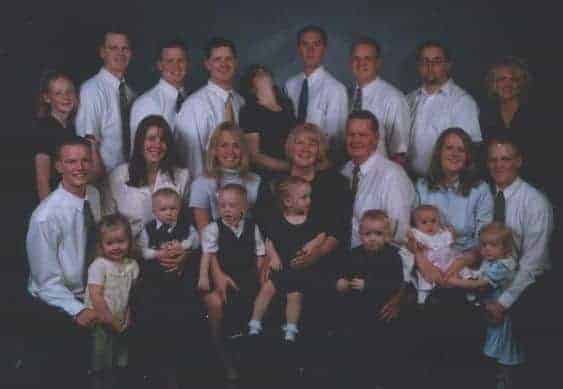 Large crowded family portrait with nineteen adults, children, and babies posing against a dark studio backdrop.