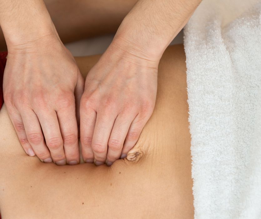 Hands pressing into the midline of a bare abdomen above the navel to check for diastasis recti.