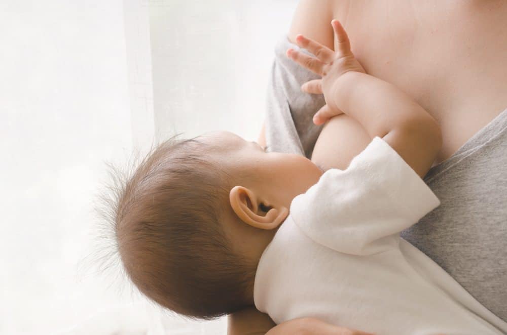 A close-up of a baby breastfeeding while resting in a mother's arms.