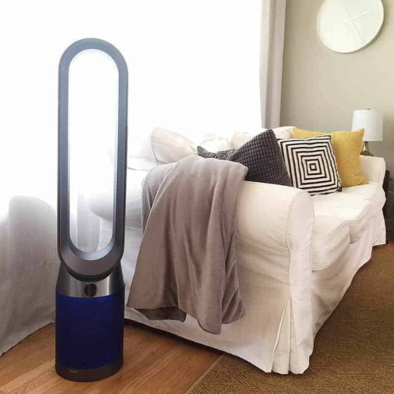 Dyson Pure Cool HEPA air purifier fan standing on a wooden floor in a living room next to a white sofa with pillows.