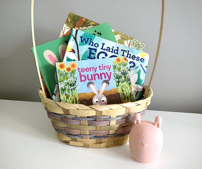 A woven Easter basket filled with several children’s board books, next to a small pink bunny egg.