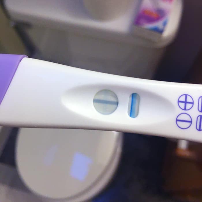 Pregnancy test showing a solid blue control line and a very faint, thin horizontal evaporation line in the result window.