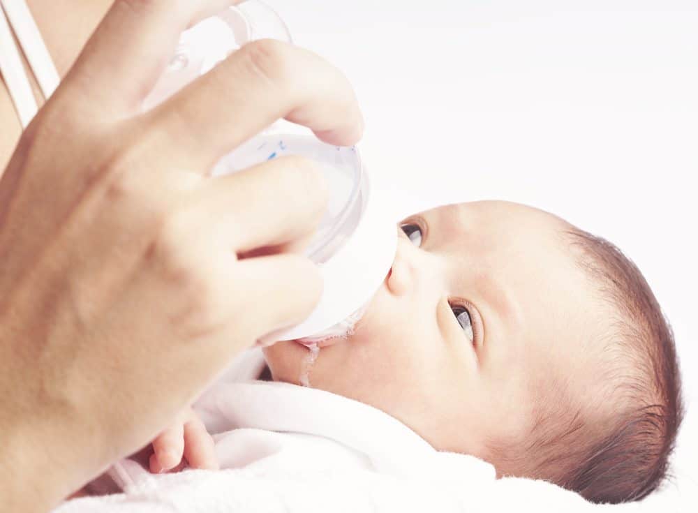 Close-up of a person's hand holding a bottle and feeding a newborn baby.