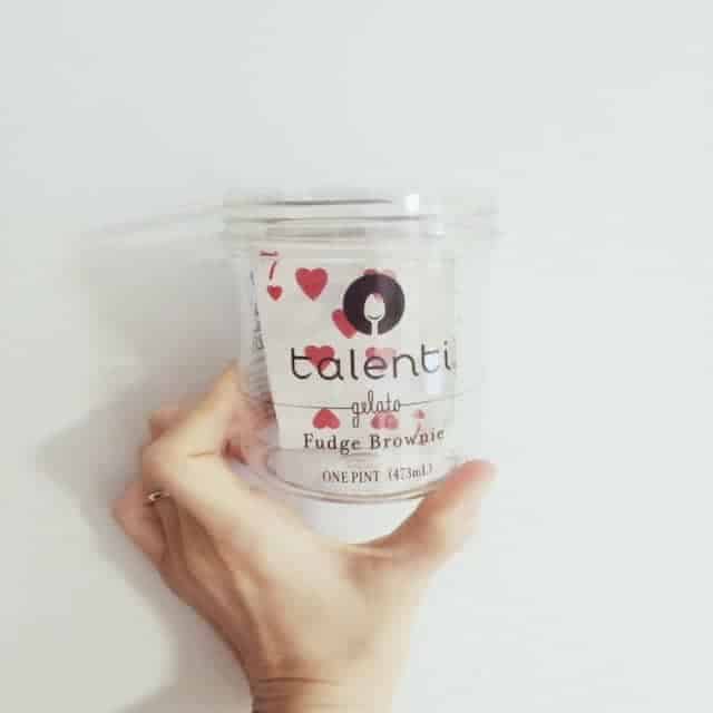 A hand holding an empty Talenti Fudge Brownie gelato container with a seven of hearts playing card inside.