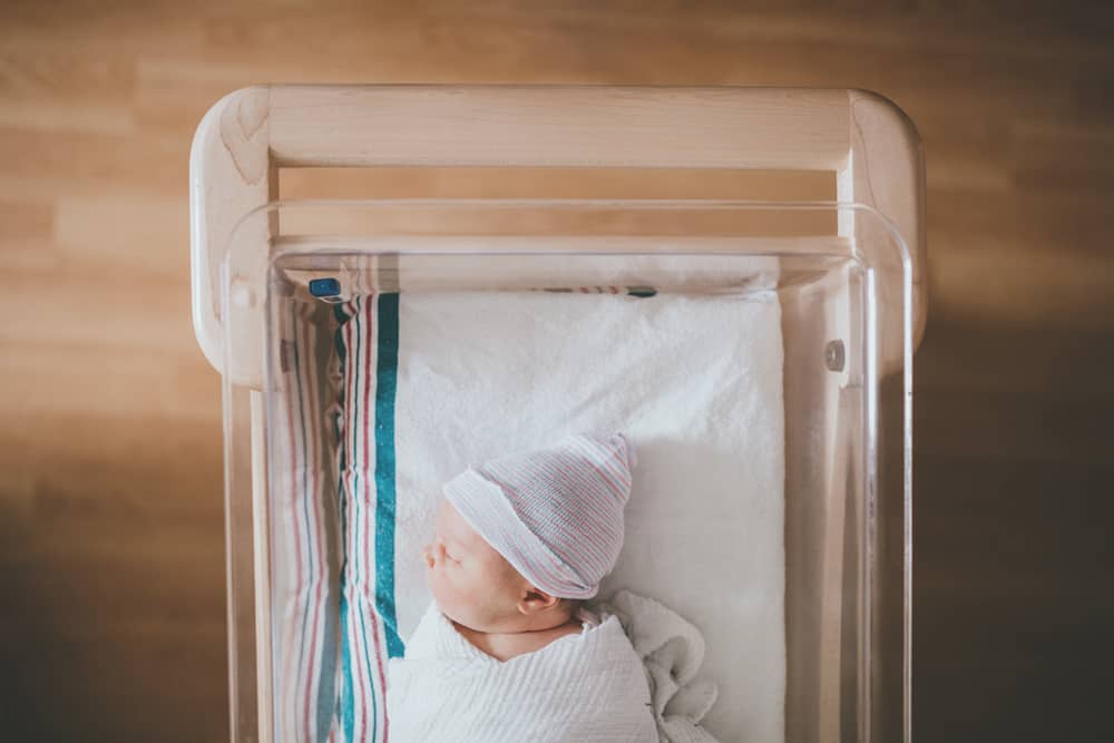 Overhead view of a swaddled newborn baby sleeping in a hospital bassinet.