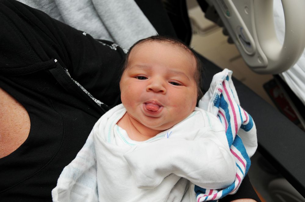 Swaddled newborn baby sticking out their tongue while being held.