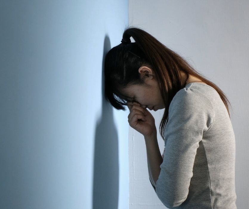 A woman leaning her forehead against a wall with her hand to her face, appearing distressed.