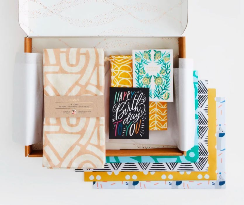 Box with a patterned tea towel, greeting cards, and assorted wrapping paper featuring colorful geometric designs.