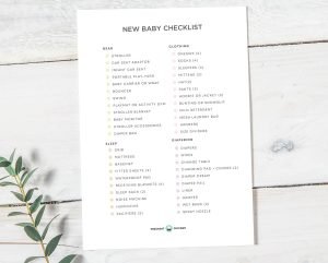 New Baby Checklist registry guide with categories for Gear, Clothing, Sleep, and Diapering on a white wood surface.