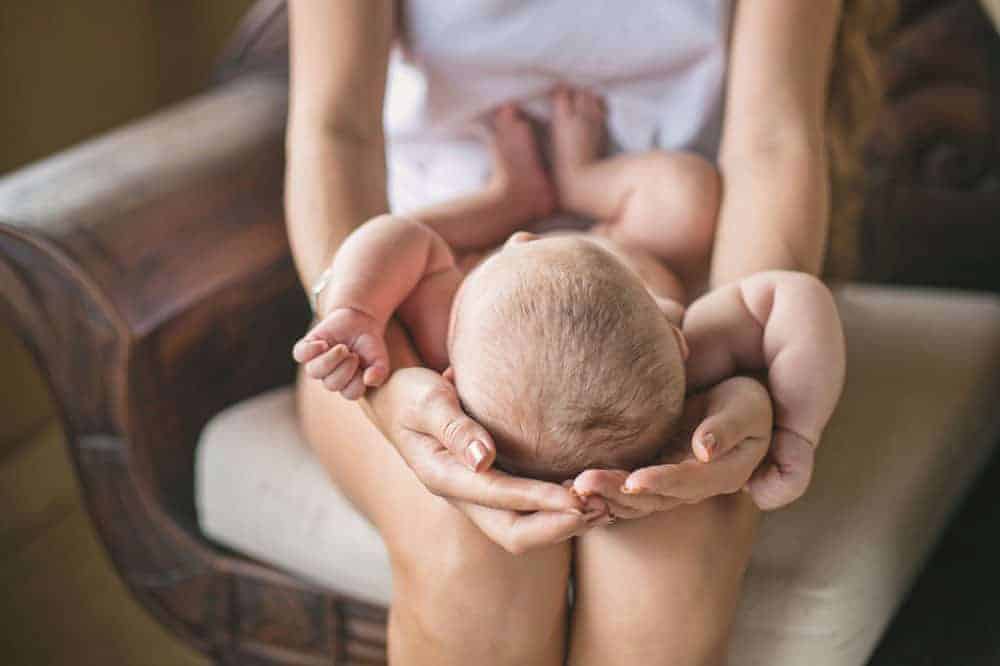 A person sitting in a chair holding a newborn baby in their lap.