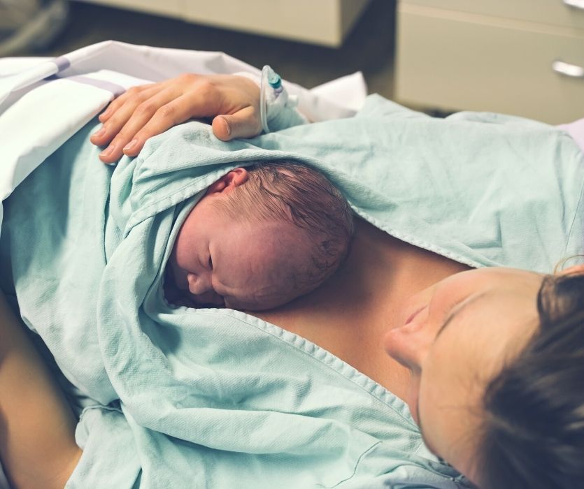 Newborn infant resting on a mother’s chest in a hospital bed for immediate skin-to-skin contact.
