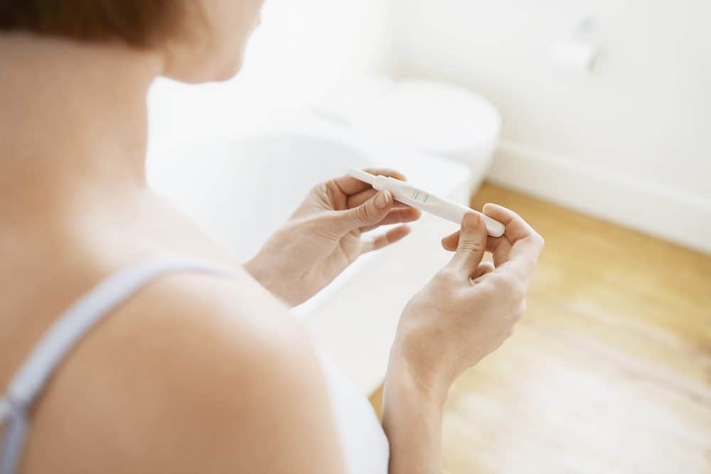 A person holding a pregnancy test with two blue lines, indicating a positive result, in a bathroom.