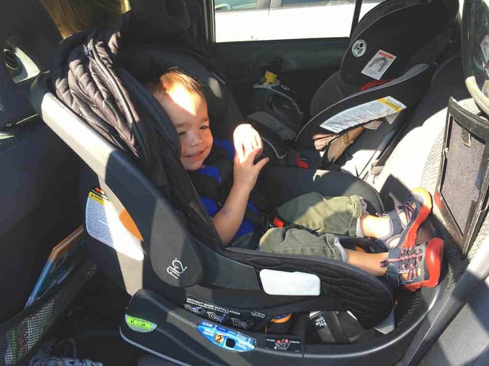 Small child smiling while sitting in a rear-facing Chicco Fit2 car seat installed in a vehicle.