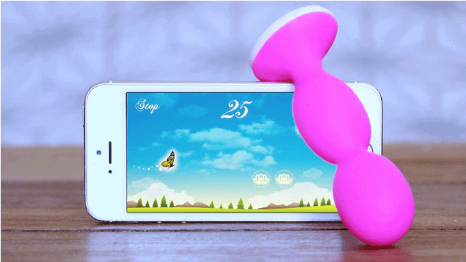 A pink pelvic floor trainer leaning against a smartphone displaying a butterfly game.
