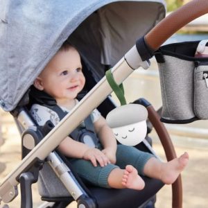 Acorn-shaped portable sound machine with a smiling face hanging from the side of a stroller with a baby inside.