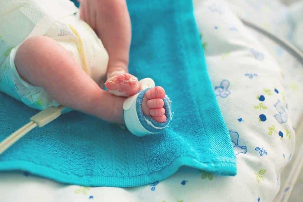 Close-up of a premature baby's feet in a NICU, wearing a pulse oximeter sensor on one foot.