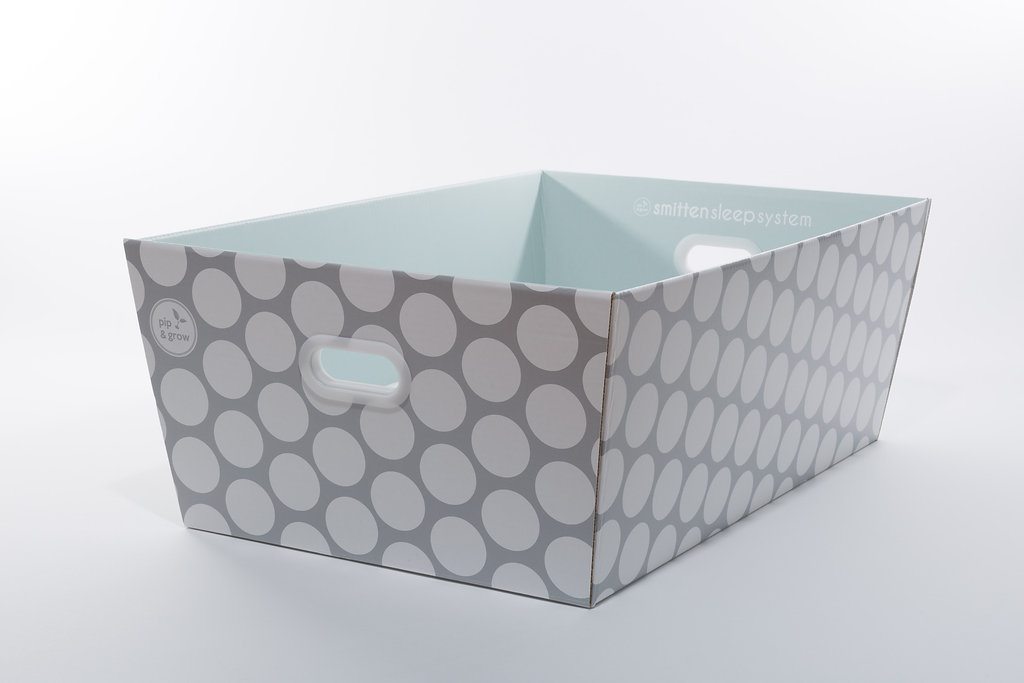 Rectangular baby box bassinet with a grey and white polka dot pattern, light blue interior, and side handle cutouts.