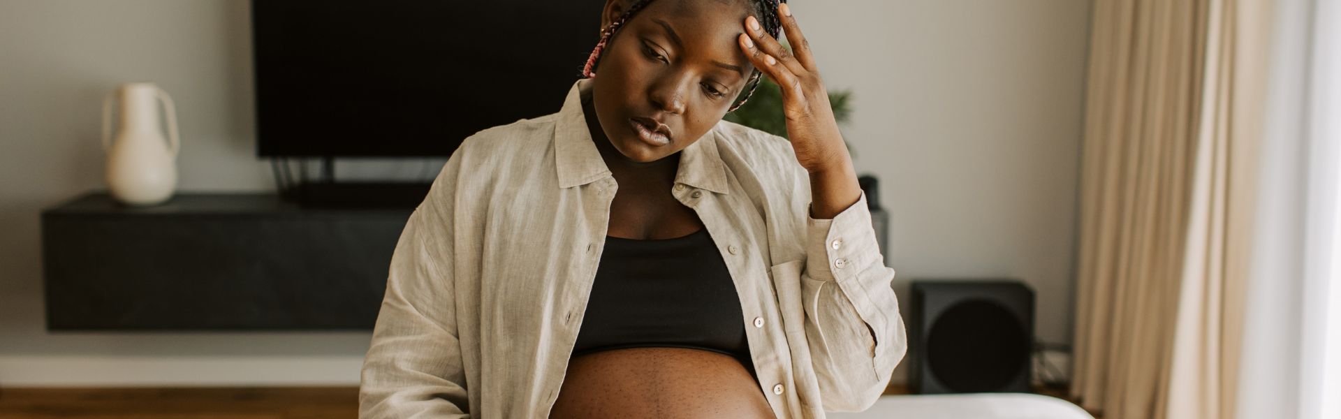 Pregnant person holding their forehead with a distressed expression.