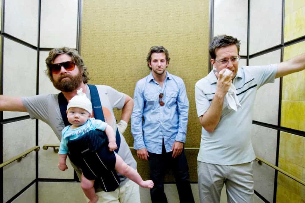Three men in an elevator from The Hangover movie; the man on the left wears a baby in a front-facing carrier.