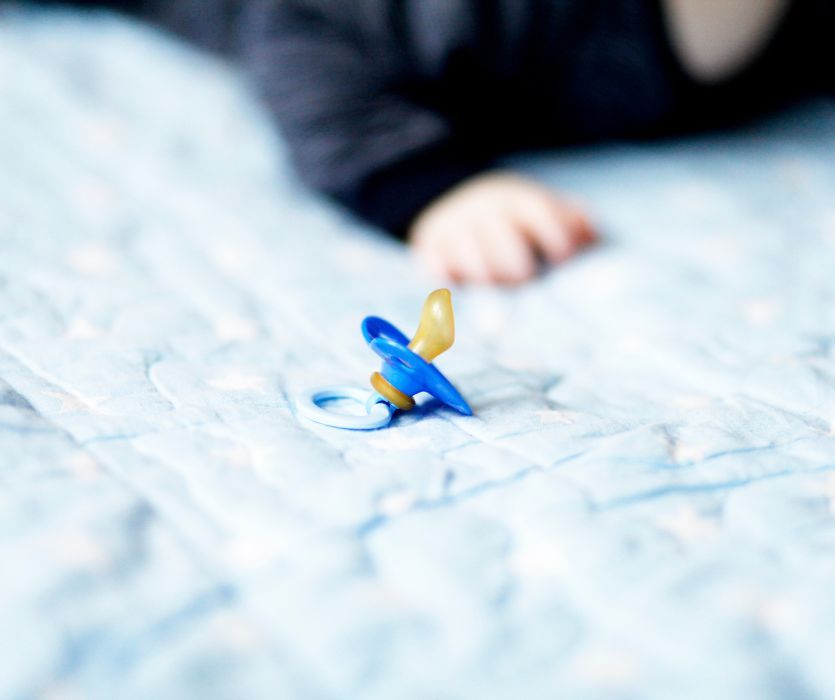 A blue pacifier rests on a star-patterned blanket near a baby’s reaching hand.