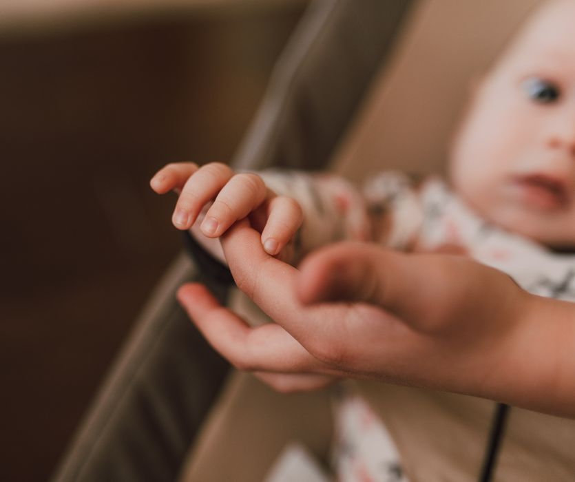 Close-up of a baby's hand grasping an adult's finger.