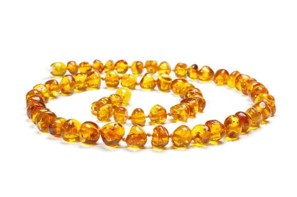 Amber baby teething necklace with polished honey-colored beads knotted individually on a string against a white background.